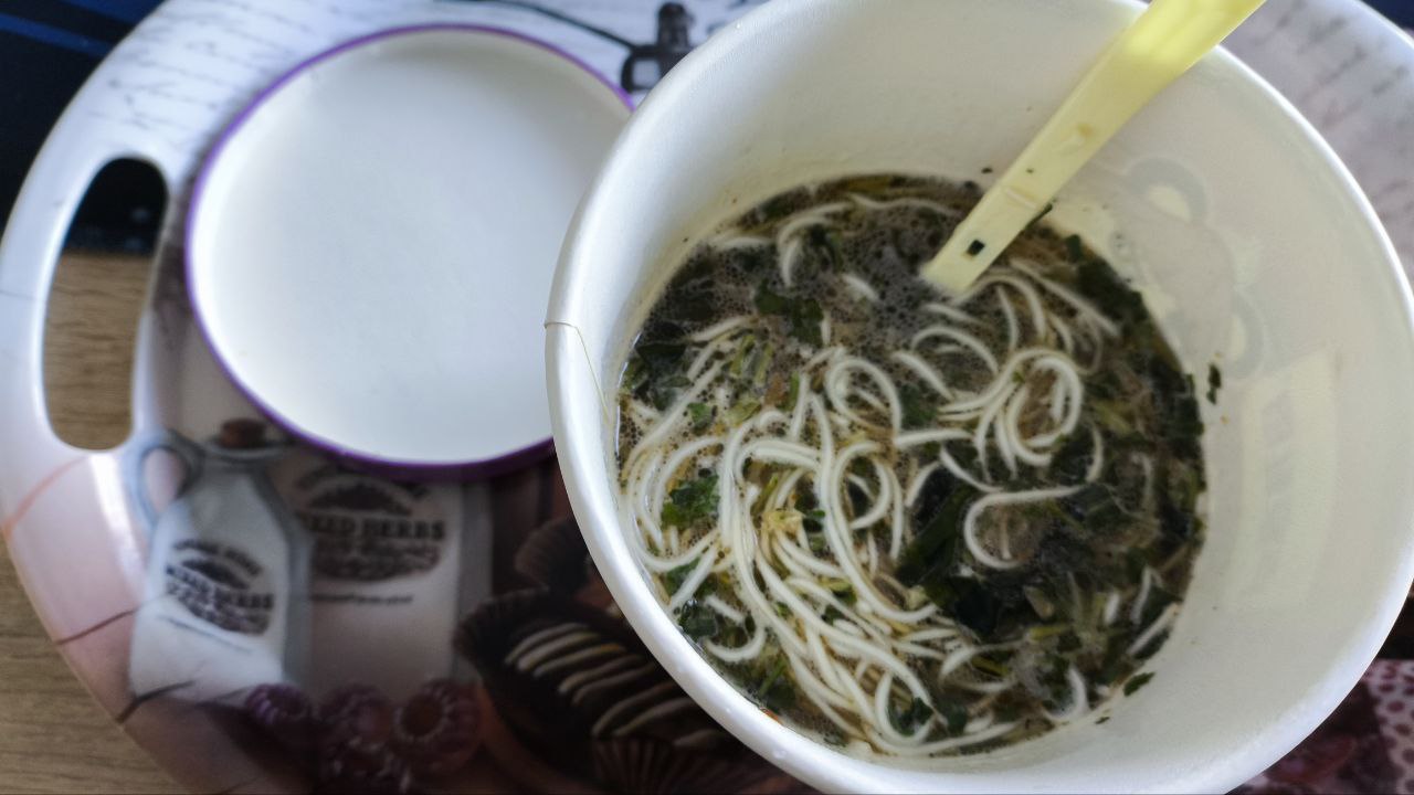 Hot Ramen with Seaweed: A Sexual Feast A seductive close-up of a cup of hot, steaming ramen noodles with tantalizing seaweed, served next to a pristine white bowl on a decorative tray.