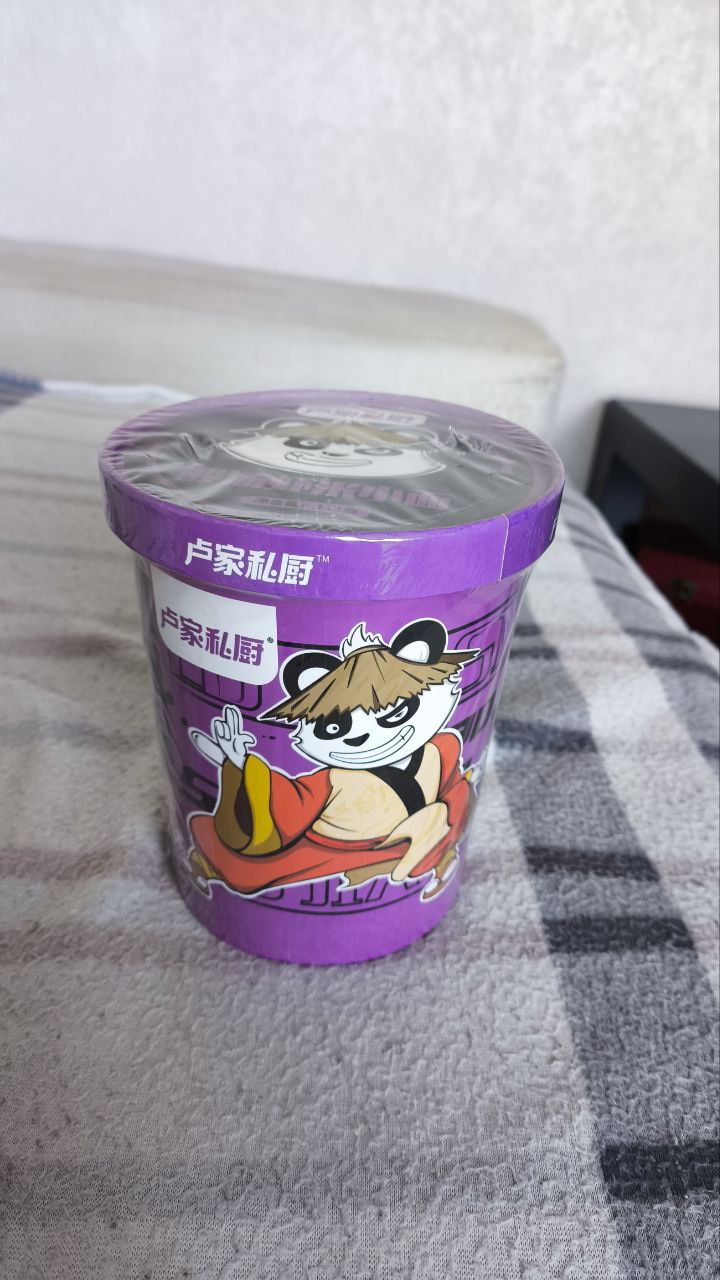 Purple Cup Noodles with Kung Fu Panda Purple cup noodles with a Kung Fu Panda character on the front. This is a very interesting object. It has a purple lid and the plastic cover over the lid. The text on the cup is written in Chinese language, but the character of the Kung Fu Panda has a distinct look. It has a happy expression on its face and looks like a warrior.