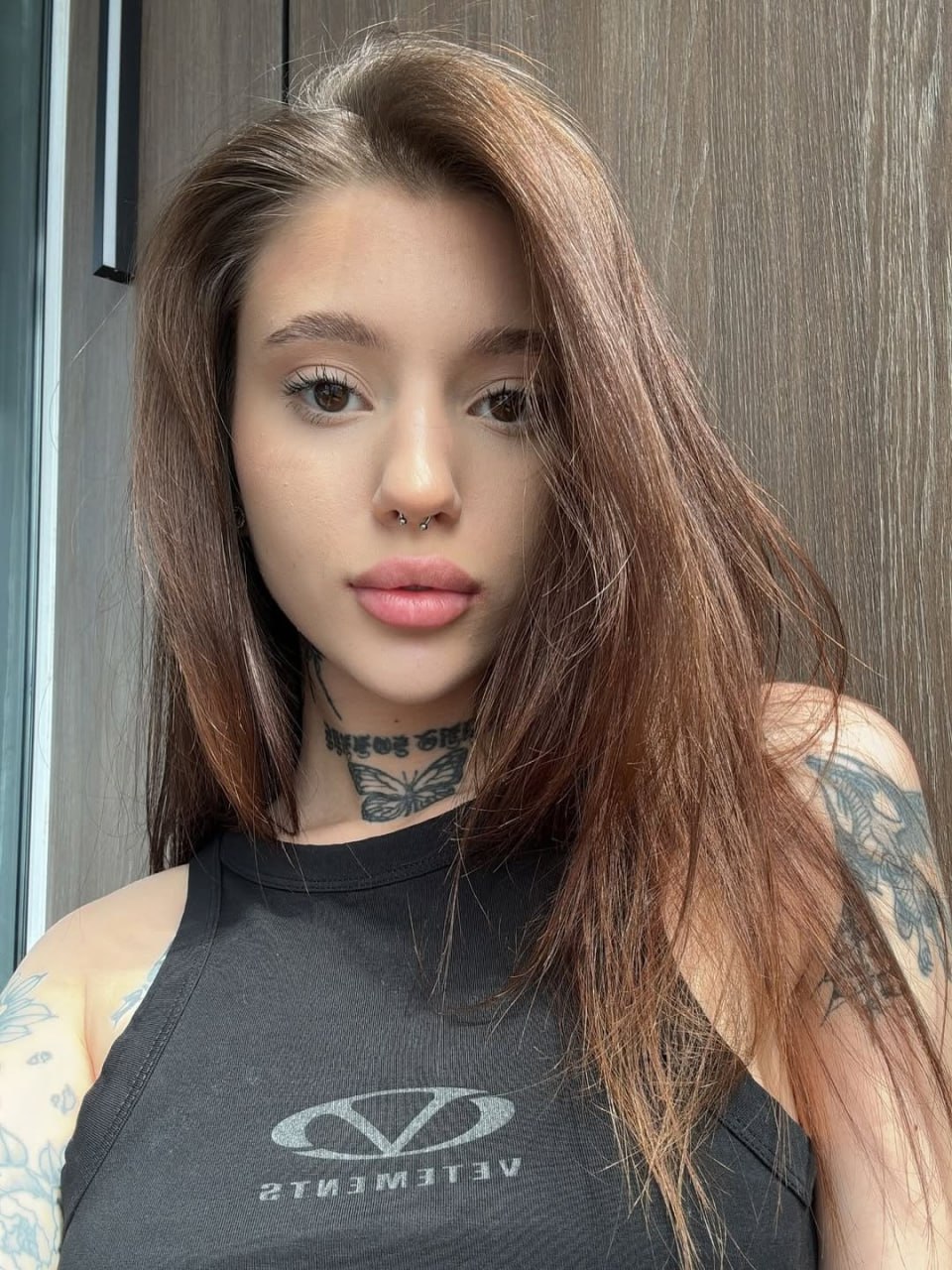 Sultry Tattooed Babe with Septum Ring Sultry close-up of a tattooed babe with piercing eyes and luscious lips, wearing a tight black tank top and a sexy septum ring. Her alluring gaze and inked skin hint at a night of pure pleasure.
